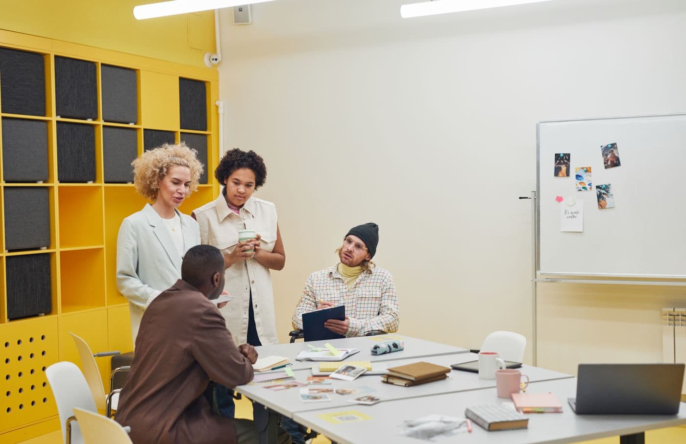 Four colleagues standing around a table in a meeting room, talking through printed work